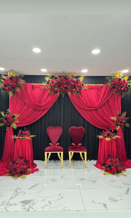 Kırmızı perdeler ve çiçeklerle süslenmiş kına tahtı ve fotoğraf köşesi.