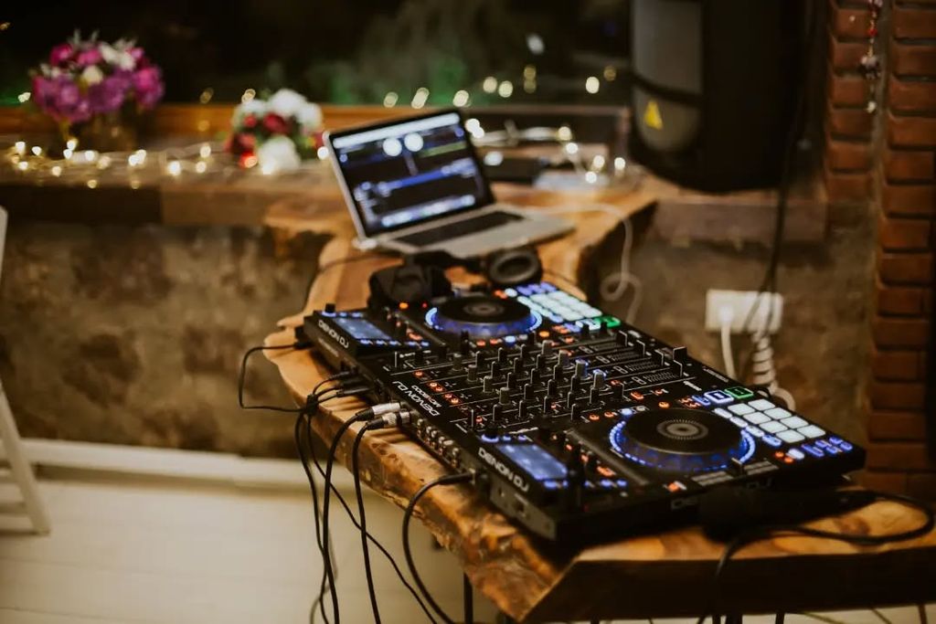 Ahşap masa üzerinde kurulu DJ mikseri ve arkasındaki laptop.
