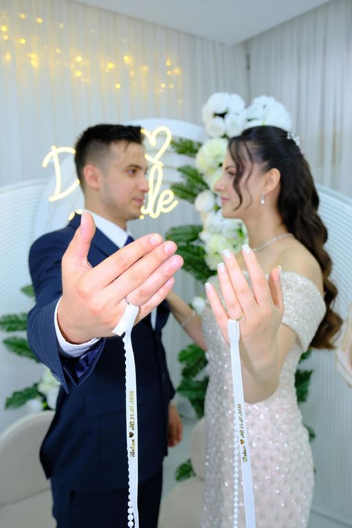 Yüzüklerini ve nişan kurdelesini kameraya gösteren gelin ve damat.