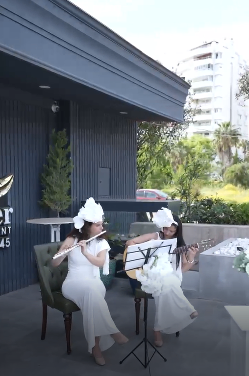 Açık alanda yan flüt ve gitar çalan beyaz elbiseli müzisyenler.