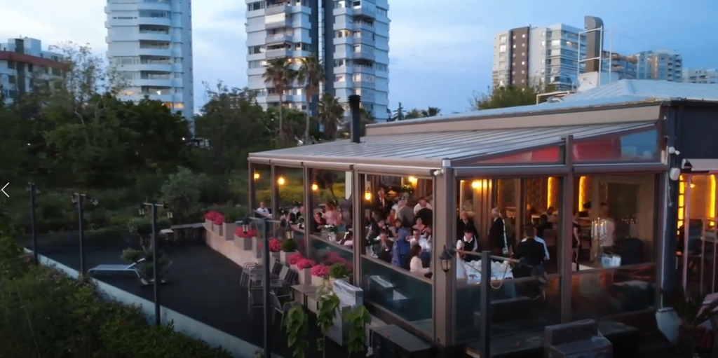 Akşam saatlerinde camlı terasında davetlilerin bulunduğu restoran mekanı.