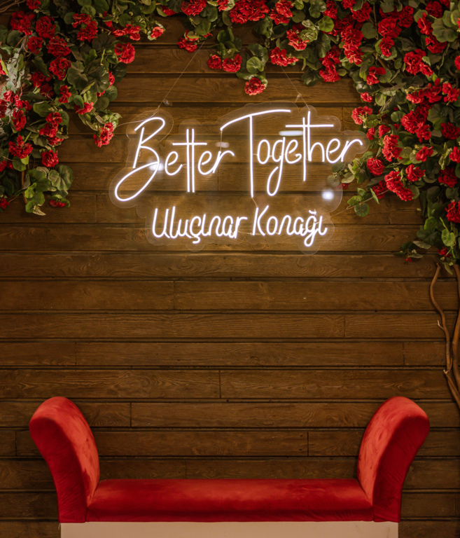 Neon yazılı ahşap duvar, kırmızı çiçekler ve kırmızı oturma bankı.