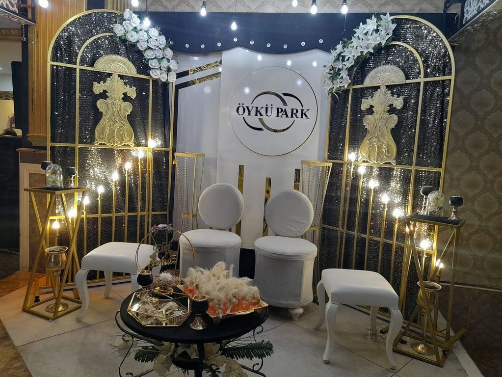 Siyah ve altın renkli arka fon, beyaz koltuklar ve tepsili nişan çekim alanı.